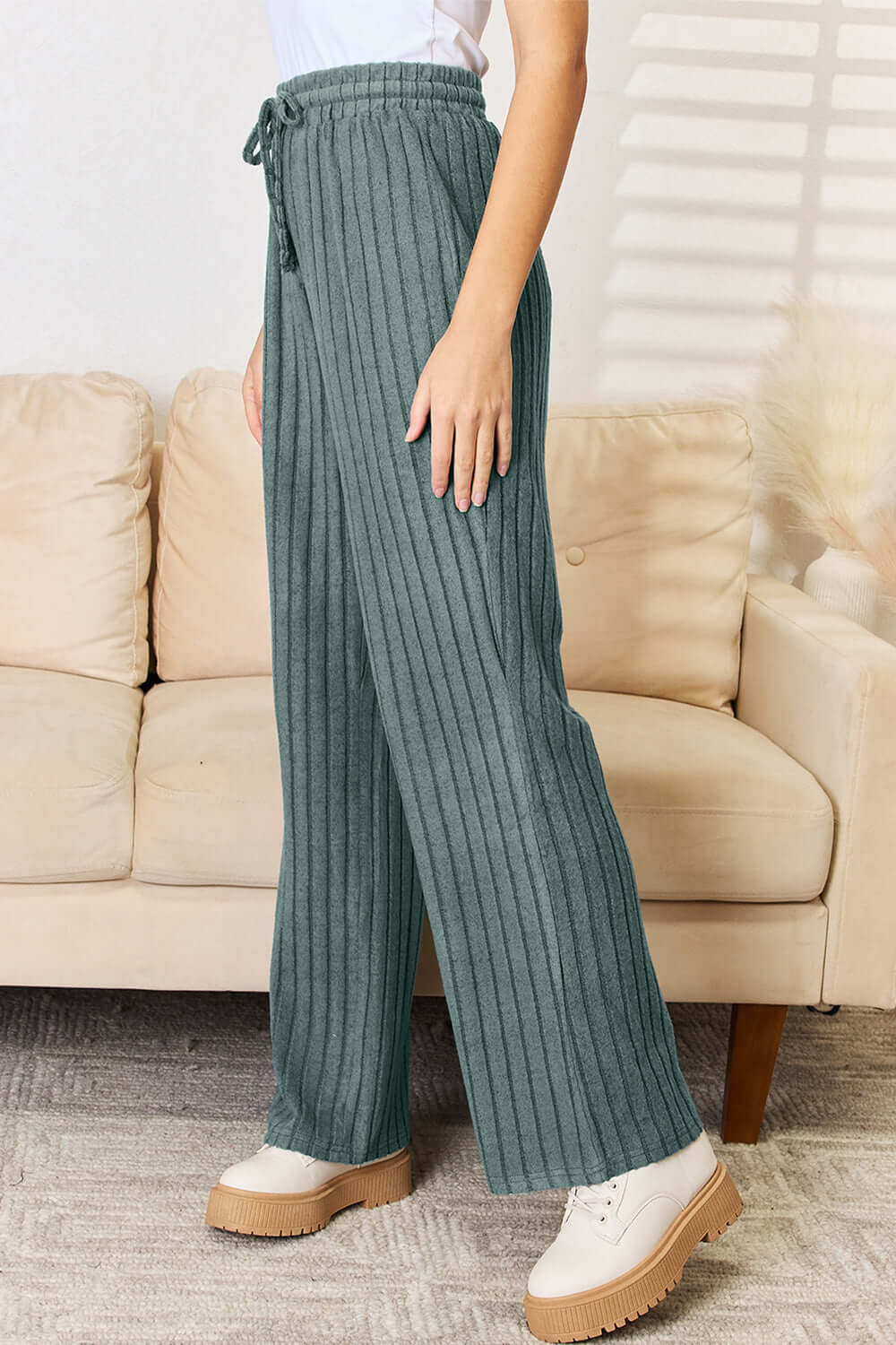 Green ribbed straight pants set with drawstring, model wearing on couch, slightly stretchy fabric.